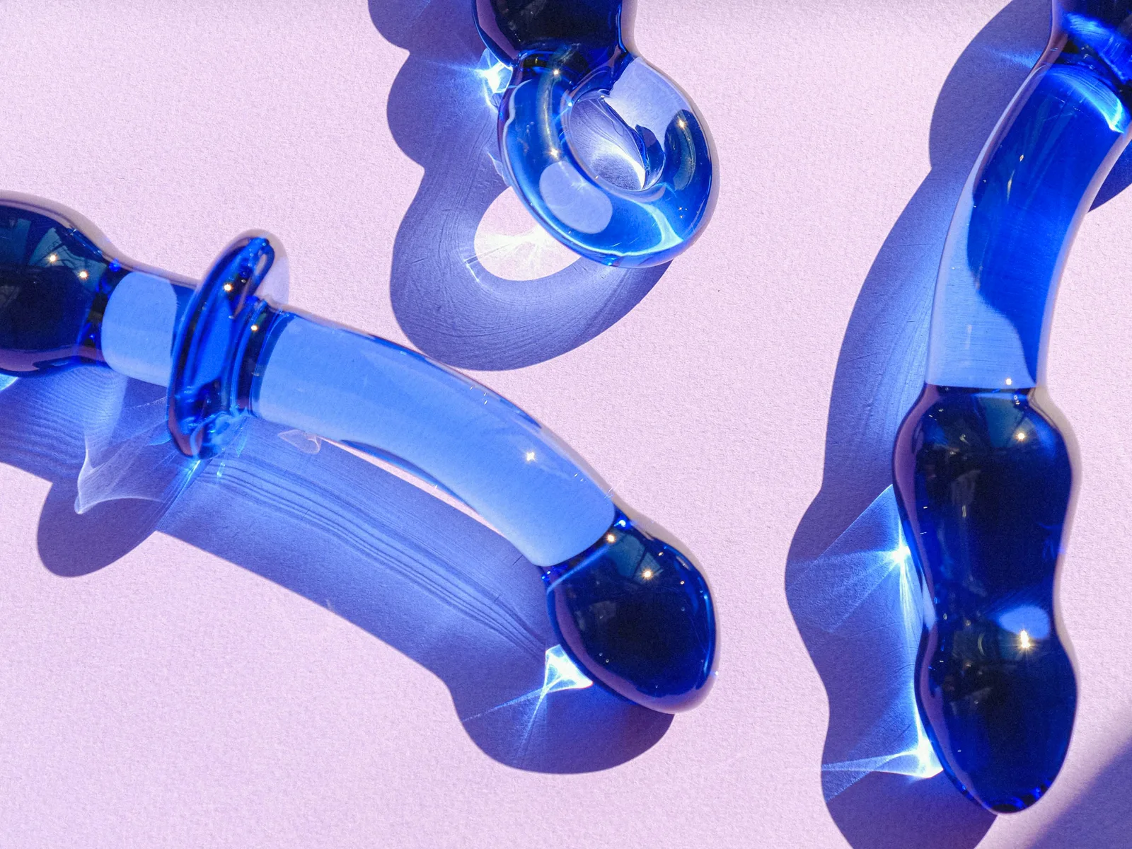 Cuatro piezas de vidrio azul sobre fondo lila, con luz dura de lado